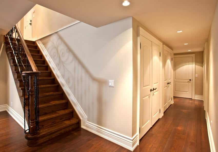 Stairs with metal railing in a hallway with white walls, dark wood floors, and recessed lighing
