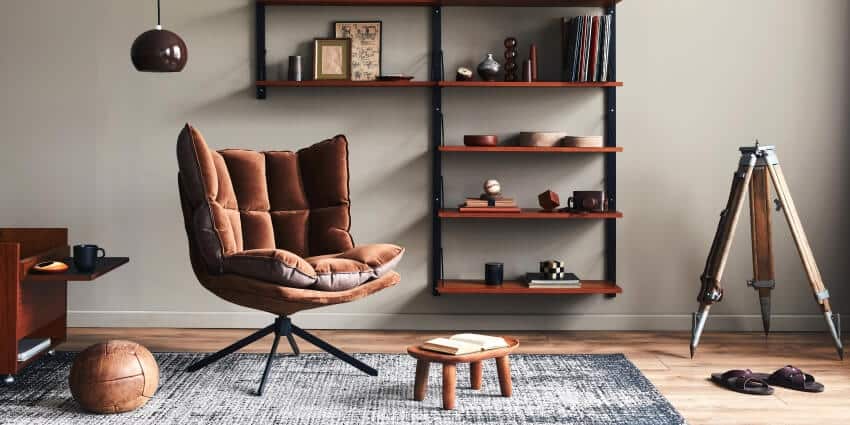 Stylish living room with dark brown armchair, wooden floating shelves, pendant lamp, and gray wall