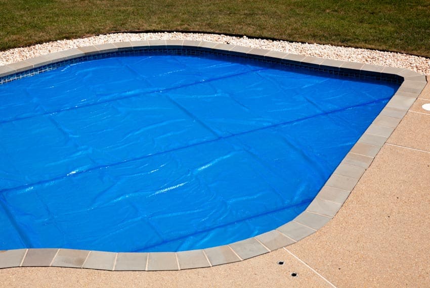Free form pool with blue cover, and tile coping
