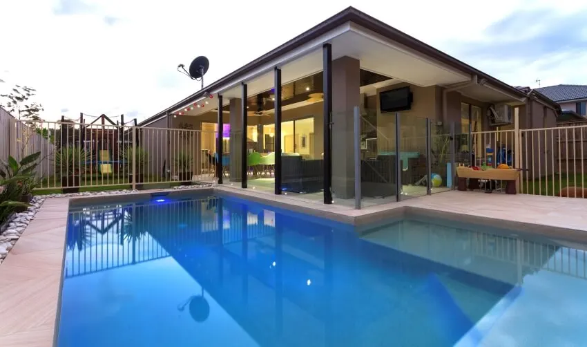 Swimming pool with color changing LED lights and railings in the backyard of a stylish home at dusk