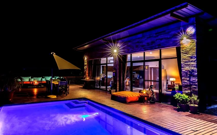 Swimming pool with LED lights and wooden deck and a fireplace on the side of a vacation house