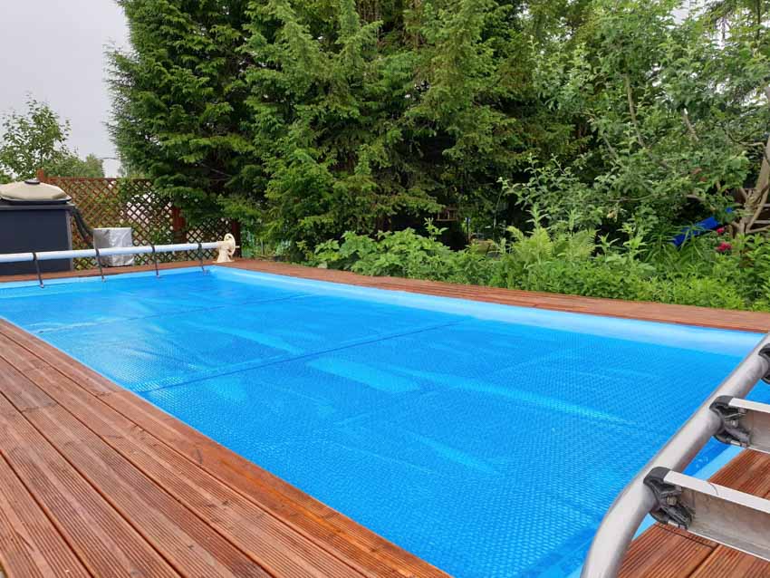 Swimming pool with winter cover, wood deck, and hedge plants