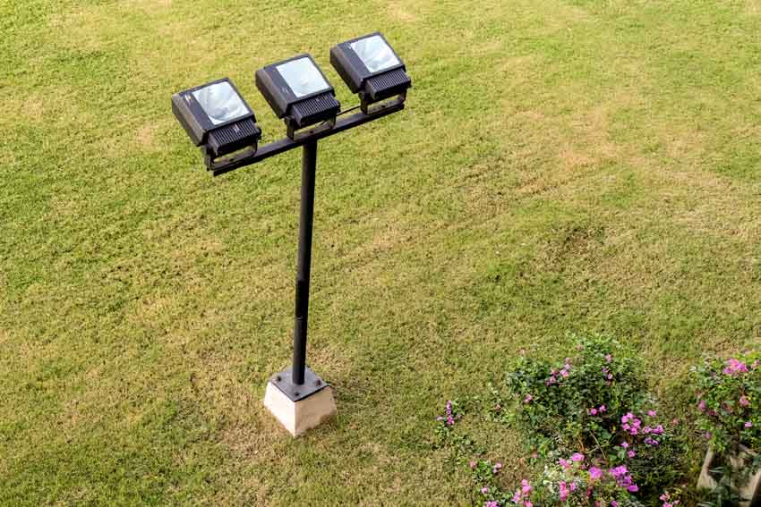 Three flood-type lights on top of a post in an outdoor area