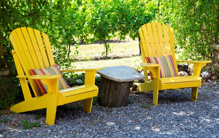 Tree trunk table in between two yellow adirondack chairs with colorful cushions
