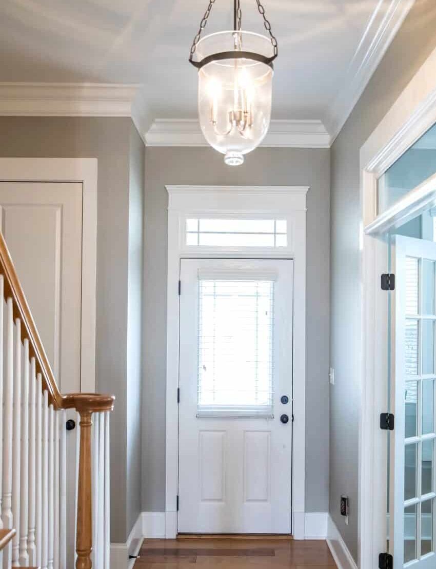 View of the front door from a hallway with hardwood floors, grey walls, and glass light chandelier