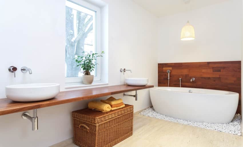 White bathroom with freestanding tub, basket storage, and two sinks on a floating wood slab countertop