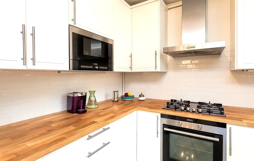 White cabinet kitchen with stainless steel appliances, tile glossy backsplash, and butcher block countertop