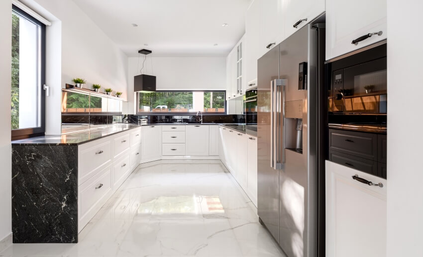 White spacious kitchen with black granite countertops, windows, and marble floor