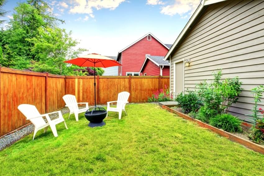 Wood fenced backyard patio with opened red umbrella and well kept lawn