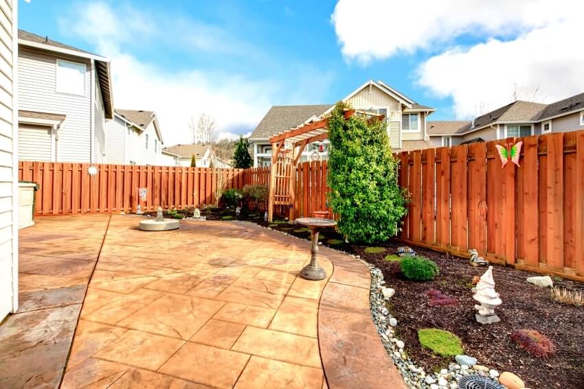 Wood fenced backyard with concrete tile floor deck and decorated flower bed