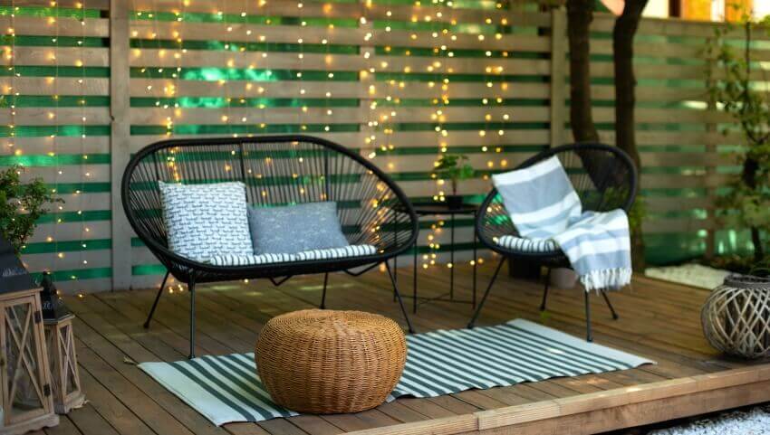 Wooden patio with chairs, pouf ottoman, and string lights on the background
