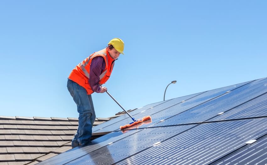 Worker cleaning solar panels on house roof