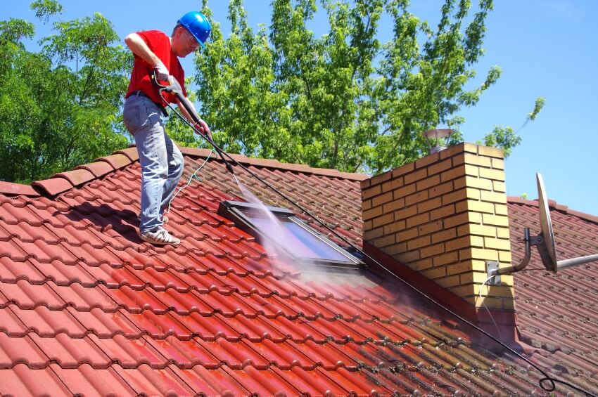 Worker on top of house cleaning tile roof with pressure tool