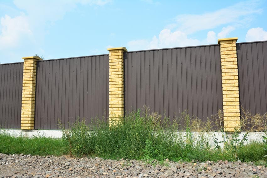 A brown metal fence with yellow brick pillars