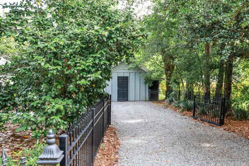 A crushed gravel driveway with metal railings, and trees surrounding it leading to a house