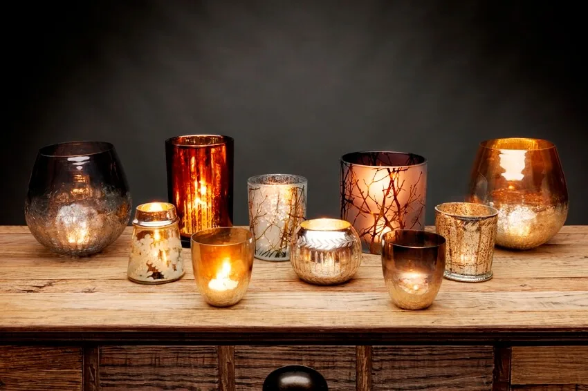 A group of glass tea light candle holders and glowing candles on a wooden table is