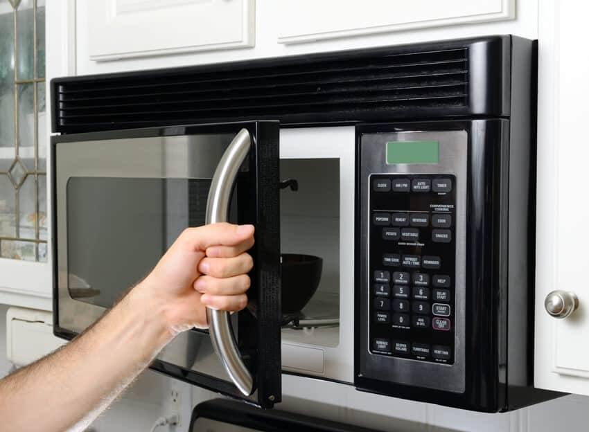 A hand opening a microwave