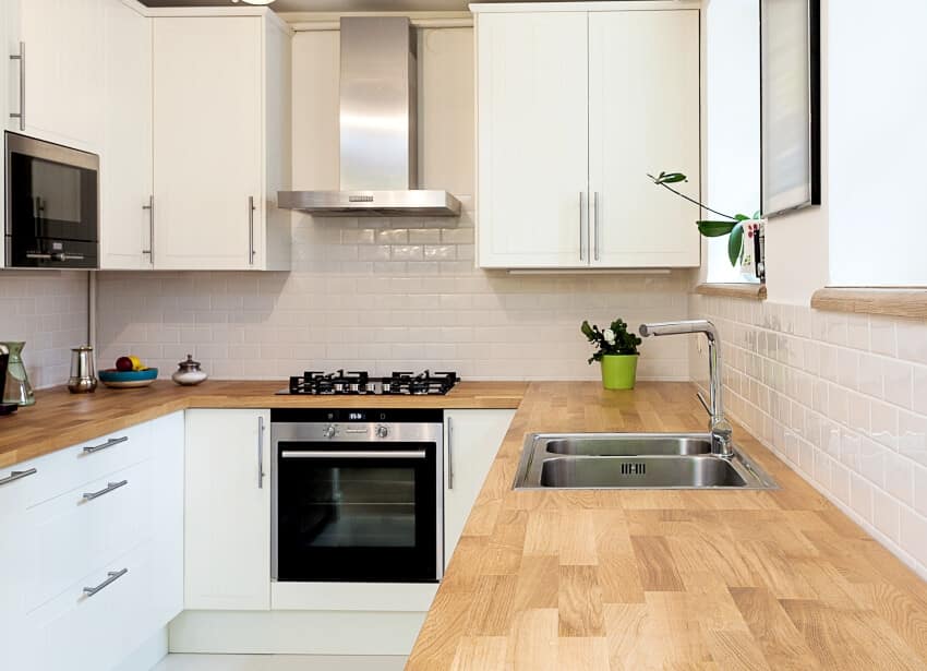 A modern wooden countertop in a white kitchen with stainless steel appliances and sink