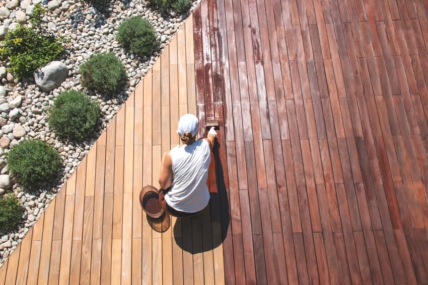 A person applying protective paint over stained wood with a brush