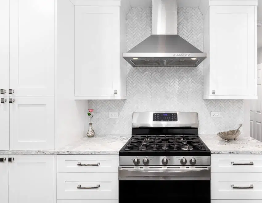 Stainless steel oven and hood in kitchen with countertops and herringbone backsplash