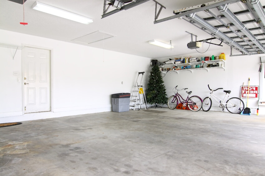 An almost empty garage with things on shelves, two bicycles, a christmas tree and storage boxes
