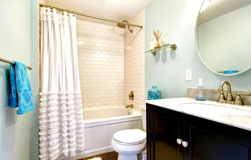Aqua bathroom with vanity with round mirror, and subway tile wall in the shower with brass fixtures