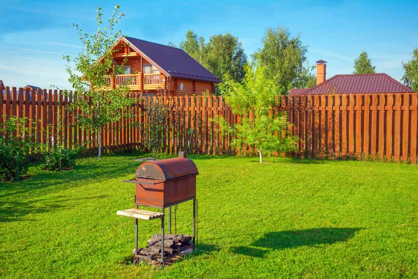 Backyard area with barbecue grill, foliage, and redwood fences