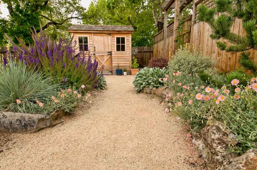 Backyard area with gravel garden, wood fence, different kinds of plants, and flowers