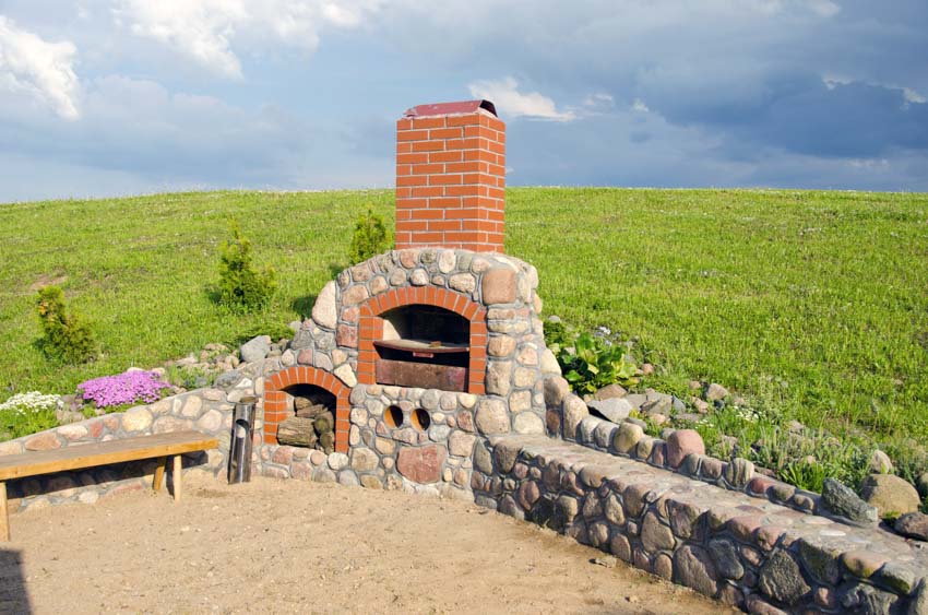 Backyard area with outdoor fireplace made of stone, pizza oven, and brick chimney