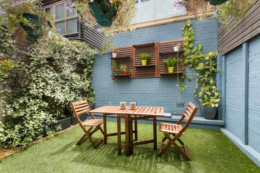 Backyard with outdoor table, chairs, plants, grassy area, and hanging shelves