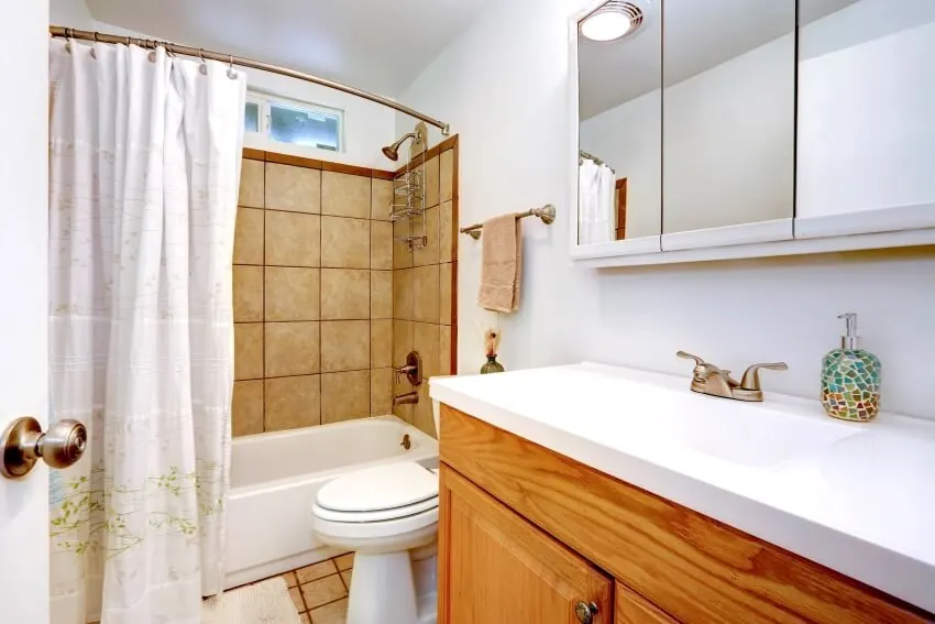 Bathroom interior with tile wall trim, brass curved shower rod, and wooden vanity cabinet