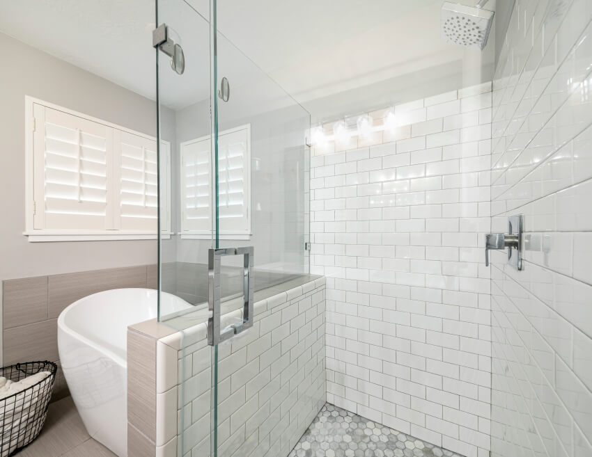Modern bathroom interior with pony wall subway tiles and glass shower and freestanding bathtub
