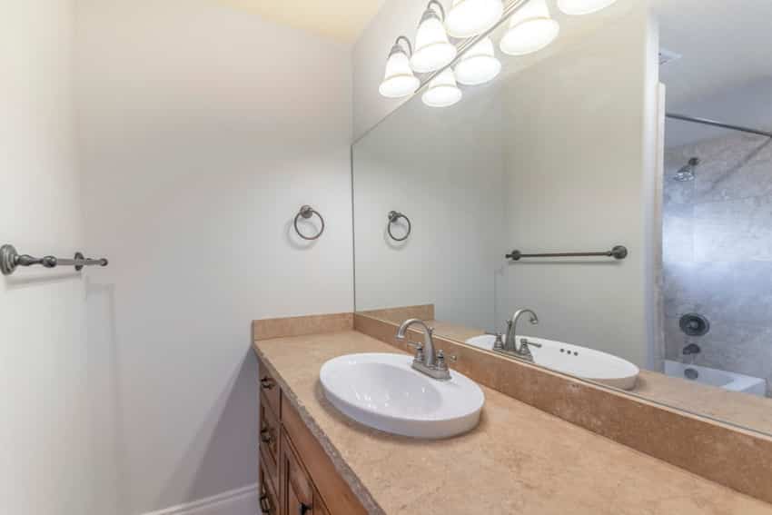 Bathroom vanity with limestone countertop, mirror, sink, and faucet