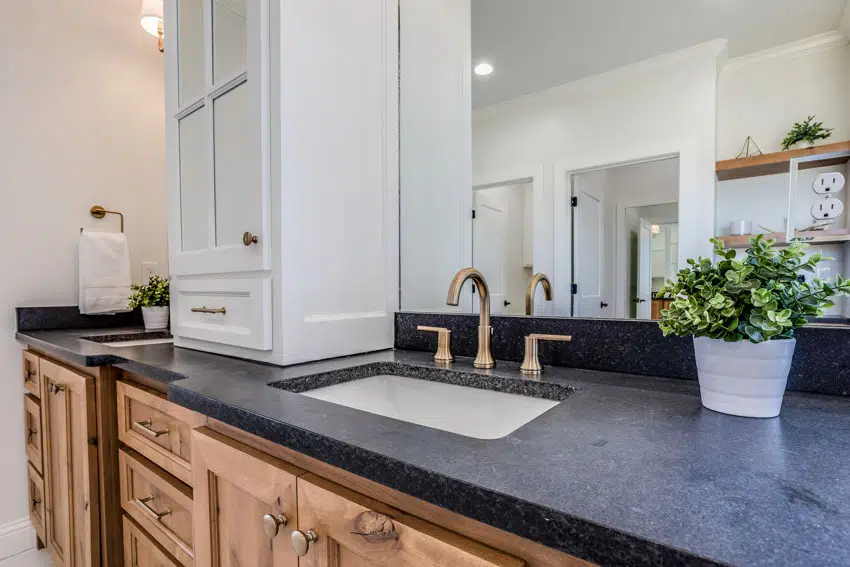 Bathroom vanity with mirror, black quartz countertop, sink, faucet, and wood drawers