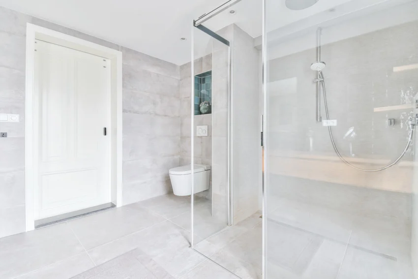 Bathroom with Carrara marble tile shower, glass door, toilet, and white door
