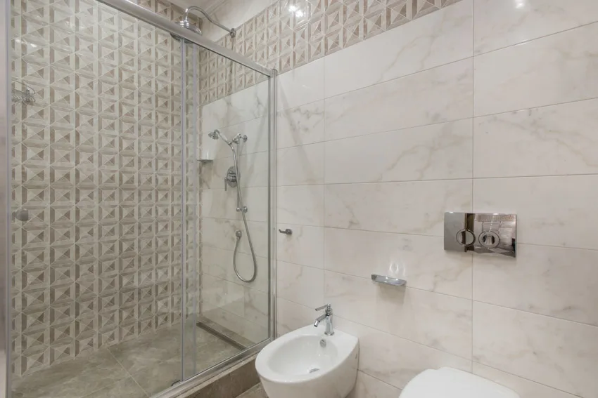 Bathroom with Carrara marble shower, toilet, shower head, tiled accent wall, and glass divider
