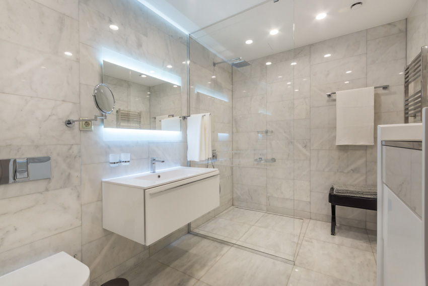 Bathroom with Carrara marble shower, vanity mirror, floating countertop, towel holder, and ceiling lights