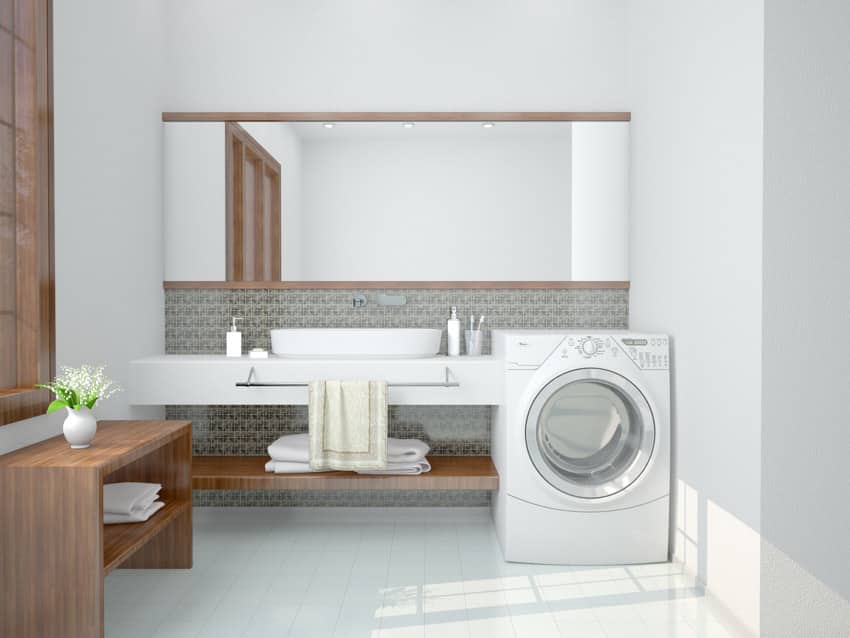 Bathroom with laundry machine, white porcelain tile floor, mirror, countertop, sink, backsplash, and faucets