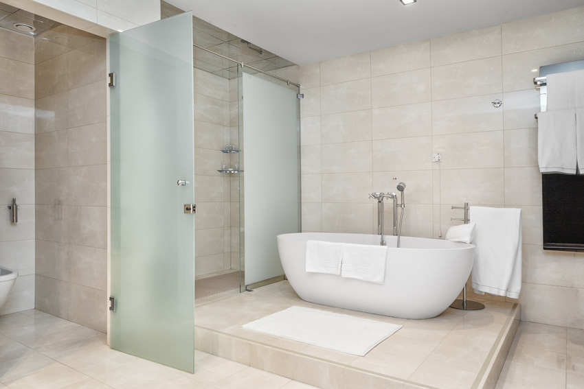Bathroom with limestone floor, walls, glass door, and bathtub