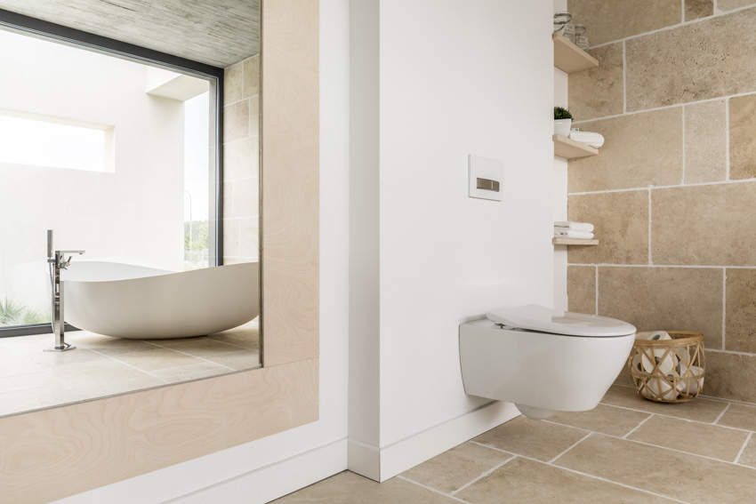 Bathroom with limestone tiles, flooring, large mirror, tub, and toilet