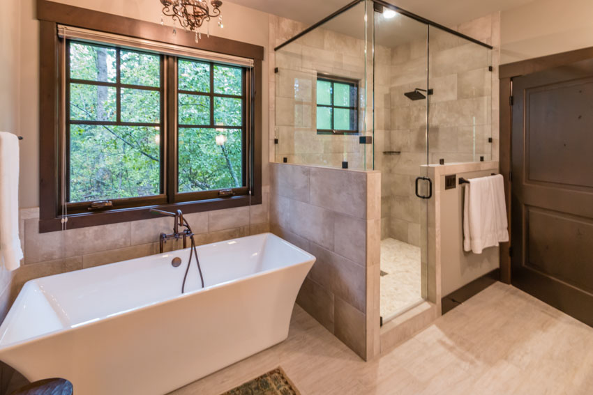 Bathroom with limestone wall, floors, glass door, shower area, tub, and window