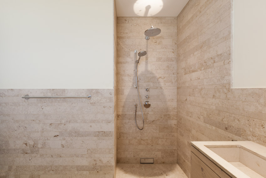 Bathroom with limestone wall, walk in shower, sink, and shower head