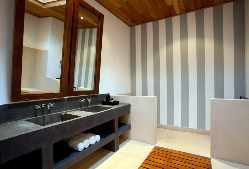 Bathroom with striped accent wall, black countertop, sinks, faucets, and mirrors