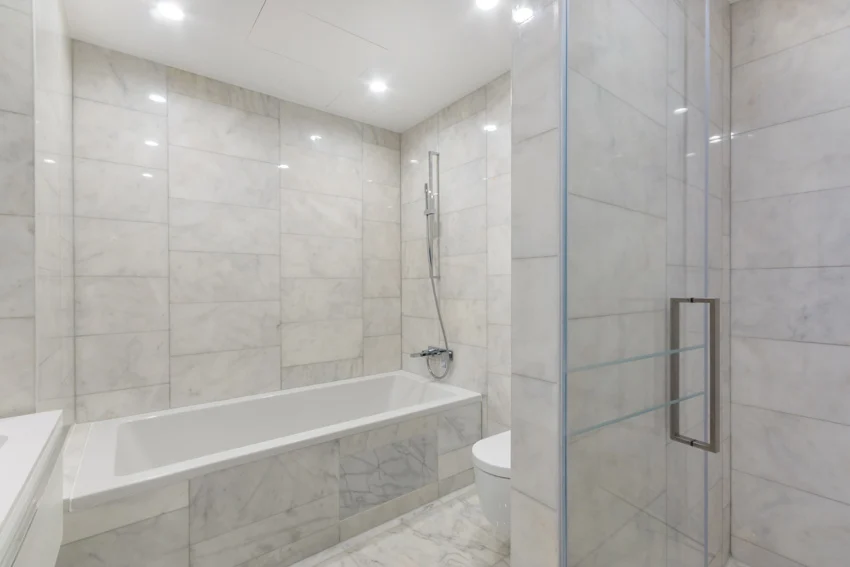 Bathroom with tub, shower head, Carrara marble tile wall, flooring, and glass door