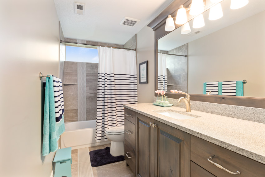 Bathroom with vanity, countertop, mirror, shower area, towel holder, toilet, and accent lighting