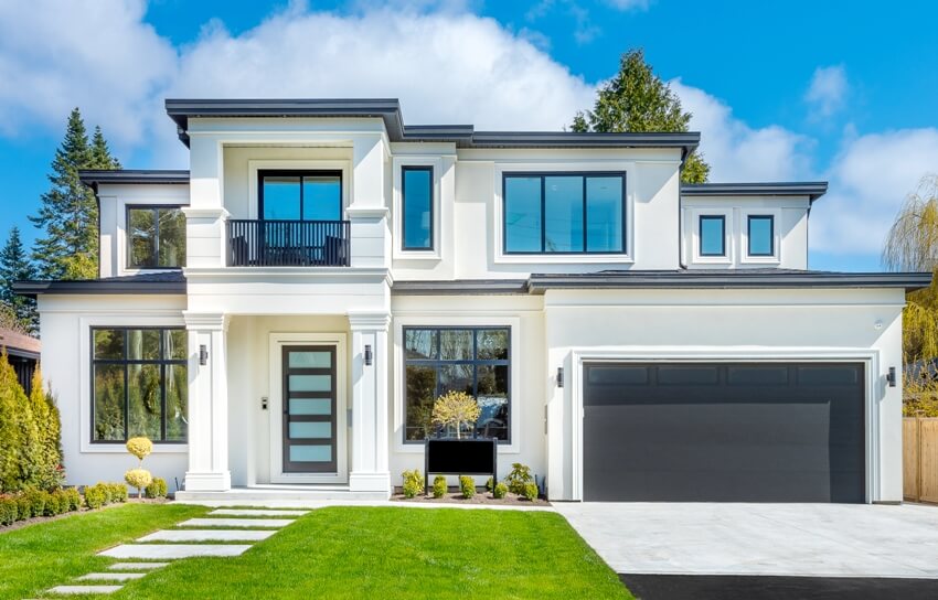 Beautiful contemporary white house with tinted windows, lush grass front yard and blue sky