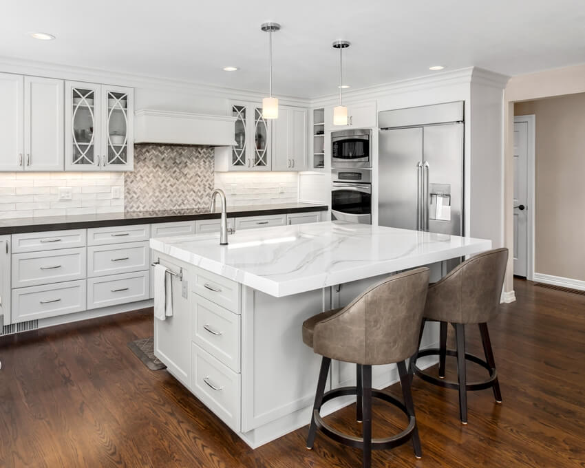A beautiful kitchen in new luxury home with appliances, hardwood floors, kitchen island with carrara marble countertop, and pendant lights