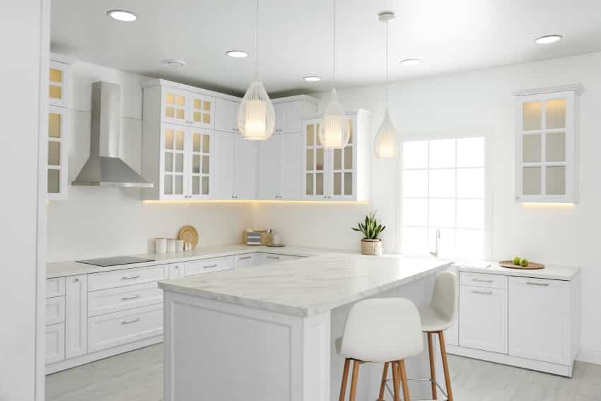 A beautiful kitchen interior with Carrara marble countertop, pendant lights and white cabinets