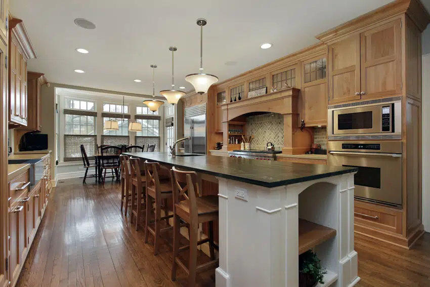 Beautiful kitchen with center island, chairs, countertop, pecan cabinets, backsplash, windows, and hanging lights