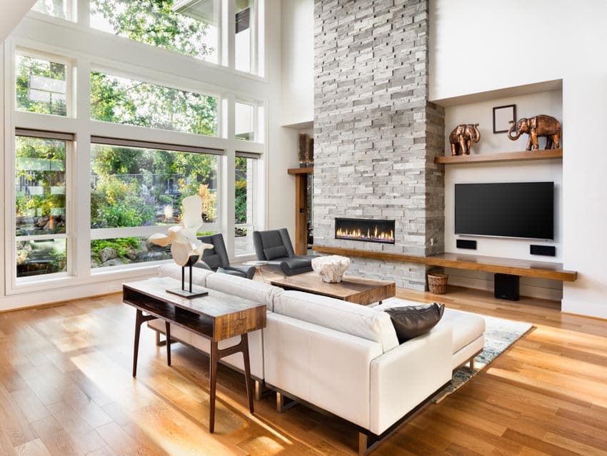 Beautiful room with wooden flooring, couch, sofa table, fireplace, television, and wall of windows